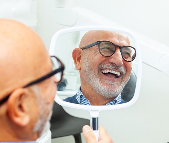 Man in glasses smiling in reflection in treatment chair