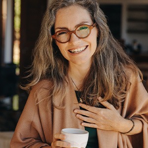 Woman with glasses smiling while drinking tea