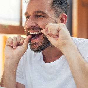 Man in white shirt smiling while flossing
