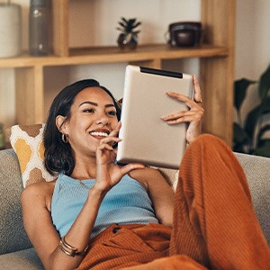 Smiling woman looking at tablet while relaxing on couch