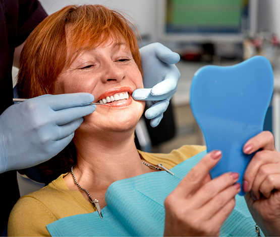 Woman in dental chair admiring her new smile in a mirror