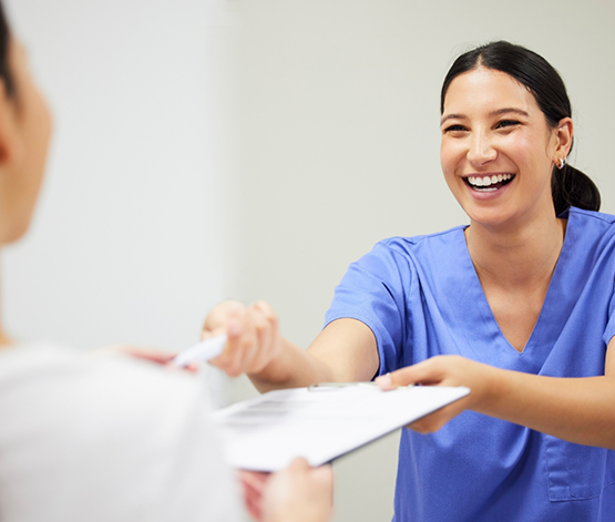 Smiling dental team member handing a clipboard to a patient