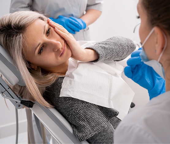 Woman holding her cheek in pain while talking to her emergency dentist in West Jordan