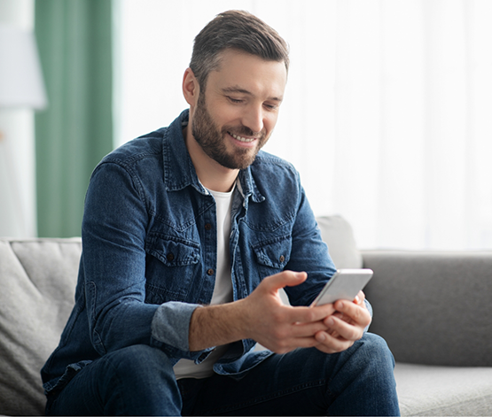 Man sitting on couch and smiling while scrolling on his phone