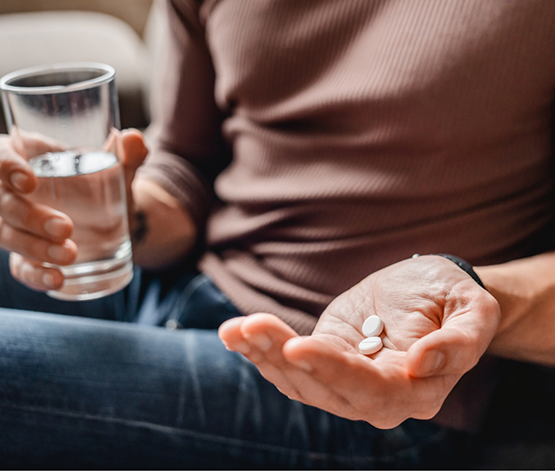 Person taking two white pills with a glass of water for sedation dentistry in West Jordan