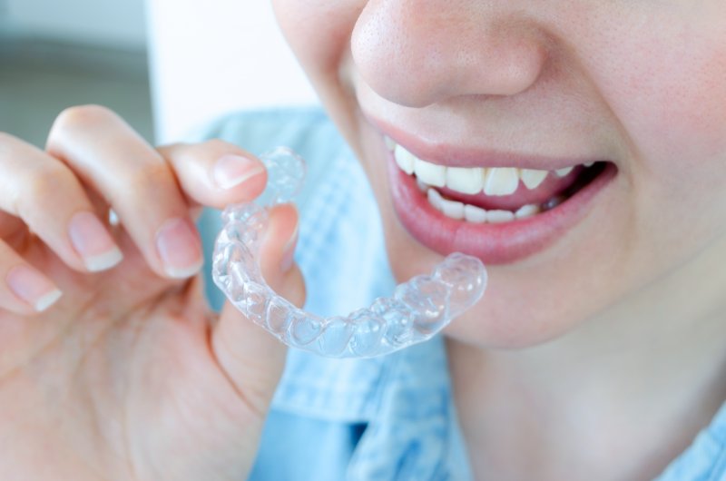 A smiling woman holding a SureSmile aligner between her fingers