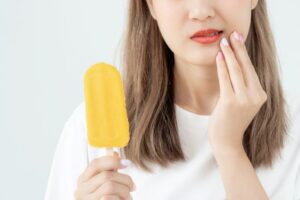 Woman grimacing as she holds ice cream bar, experiencing dental sensitivity 