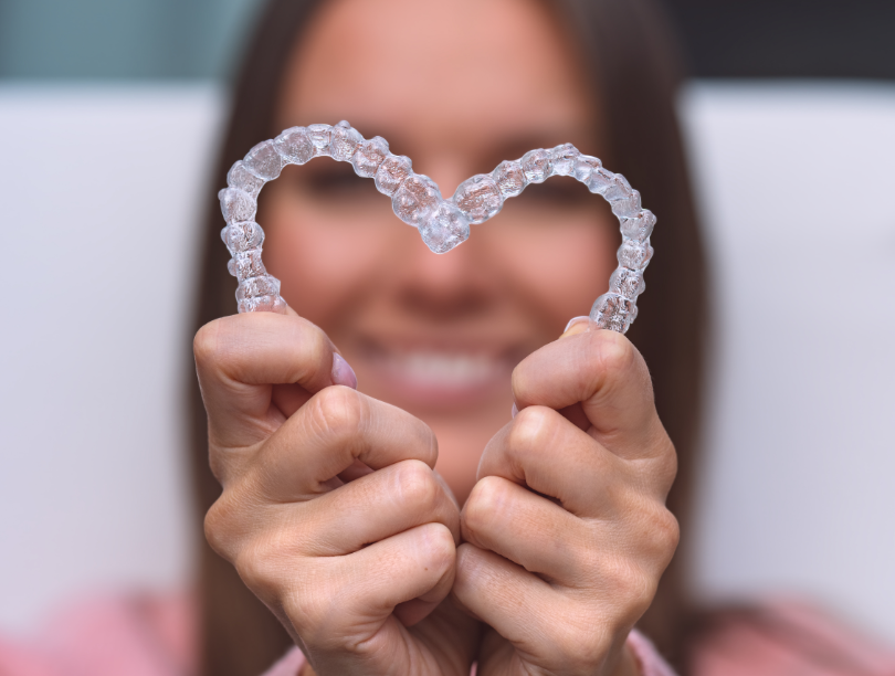 Woman holding clear aligners up in heart shape